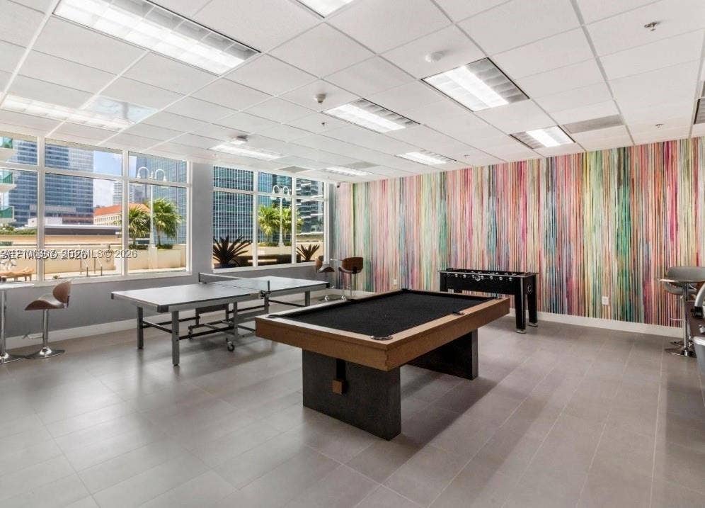 Large-format floor tile, multi-pane floor-to-ceiling windows, drop ceiling with recessed lighting, and a decorative accent wall