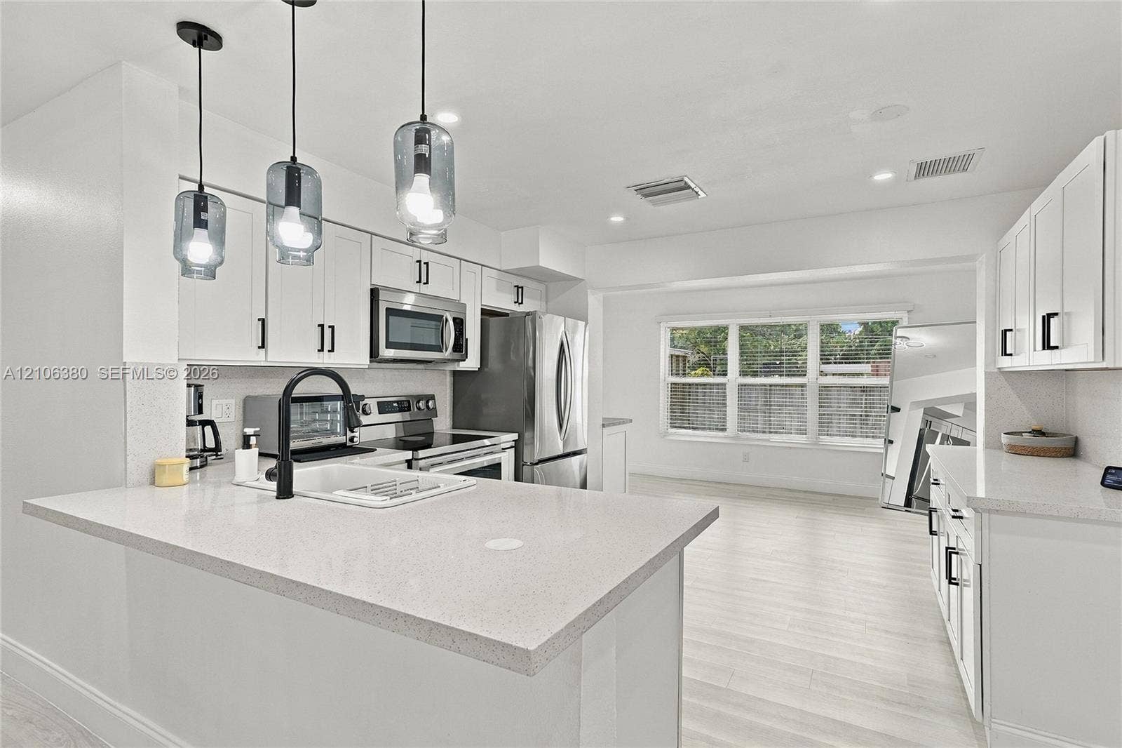 Kitchen featuring white cabinetry, solid-surface countertops, stainless steel appliances, a farmhouse-style sink with a matte black faucet, and glass pendant lighting