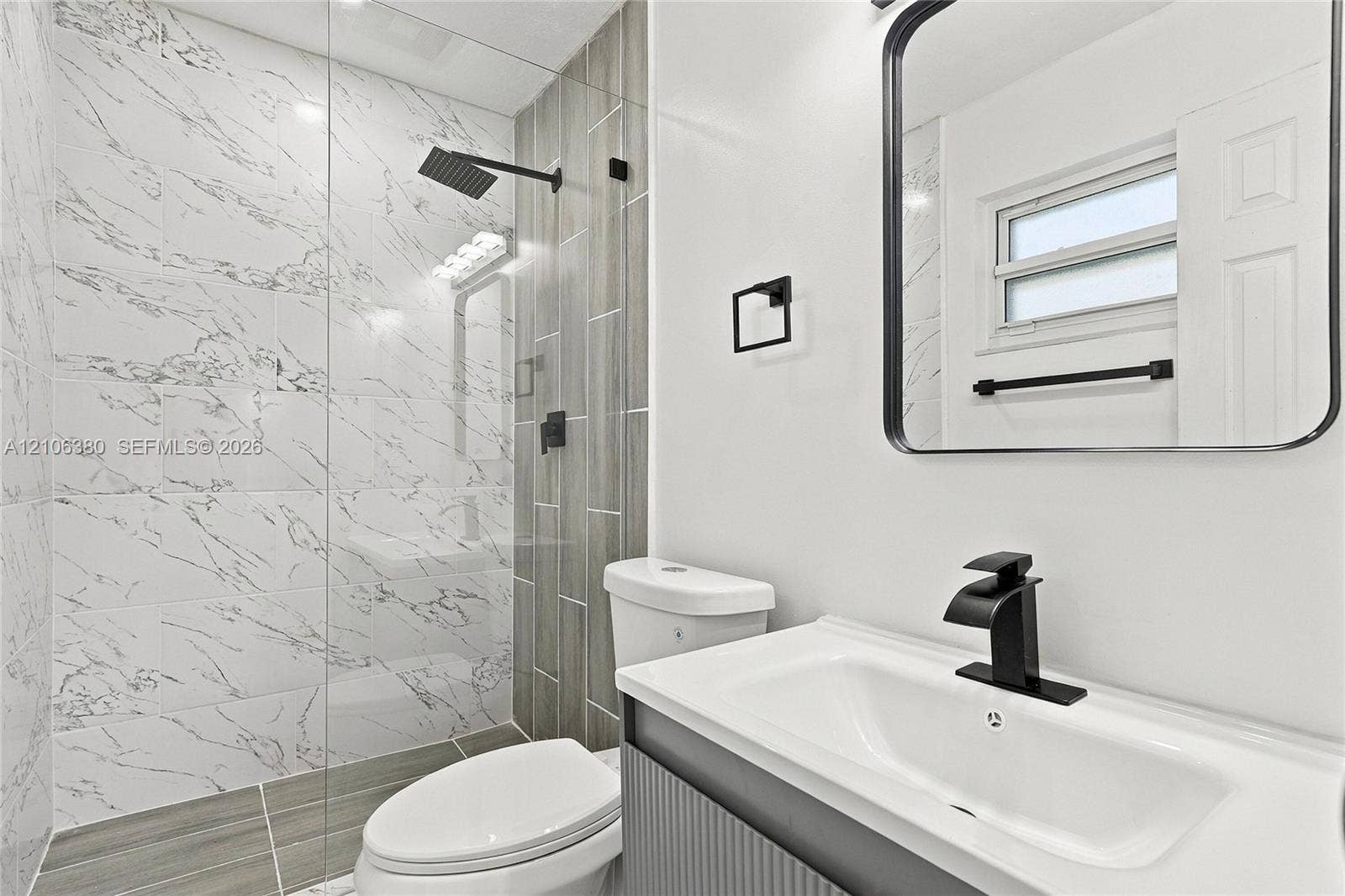 Bathroom featuring a glass-enclosed shower with marbled tile, a rain-style showerhead, wood-finish wall tile accents, a vanity with a rectangular basin and matte black faucet, and a black-framed mirror