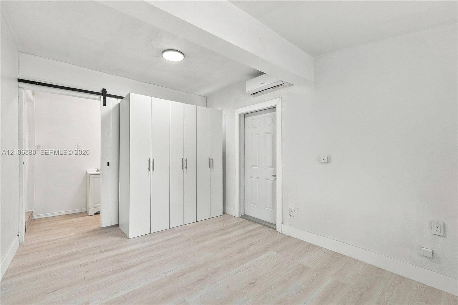Interior space featuring light-toned wood-finish flooring, white built-in cabinetry, a sliding barn-style door, and a wall-mounted climate control unit