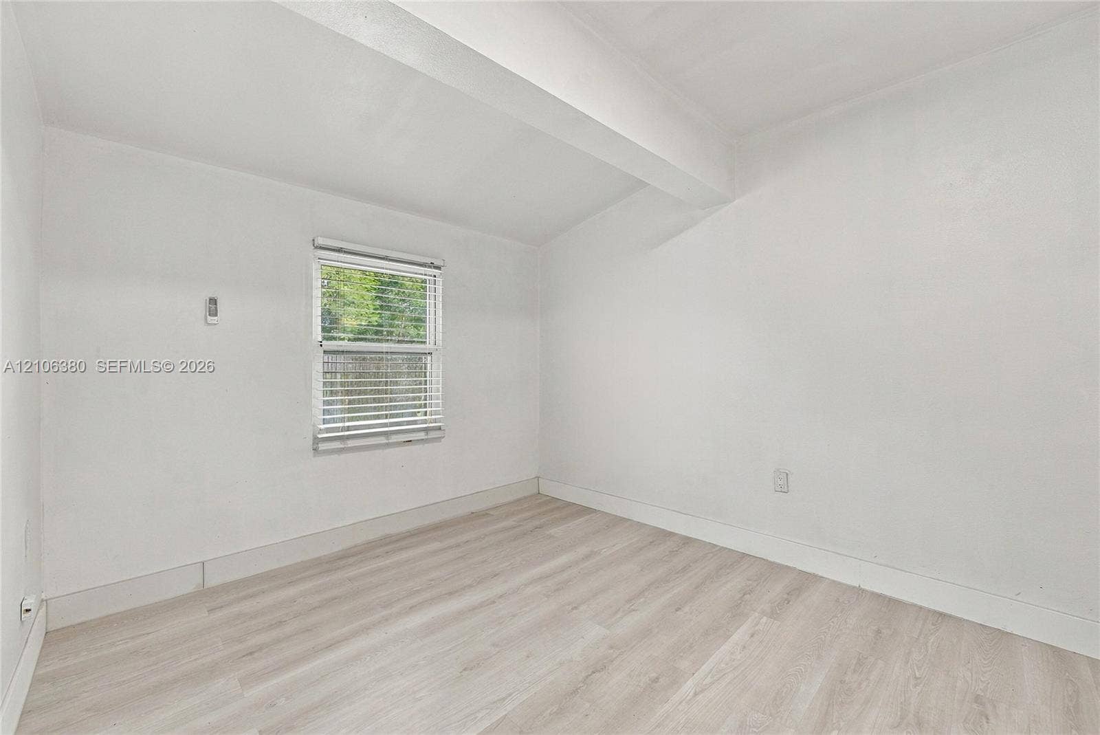 Interior room featuring wood-finish flooring, a single-pane window with adjustable blinds, and smooth-finish walls