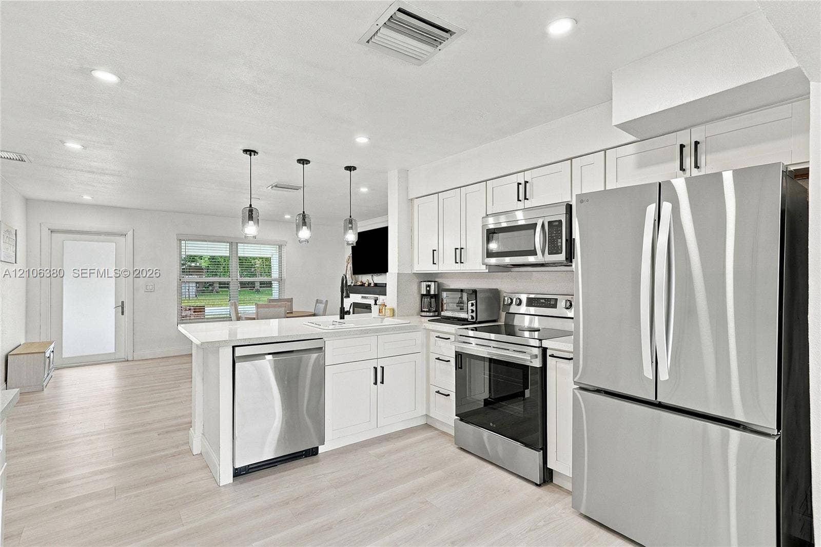 Kitchen featuring white shaker-style cabinetry, stainless steel appliances, quartz countertops, a peninsula with pendant lighting, and light-toned wood-finish flooring