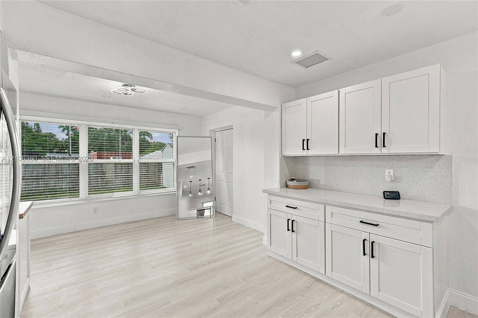 White cabinetry with matte black hardware, stone-finish countertops, light wood-finish flooring, and multi-pane windows