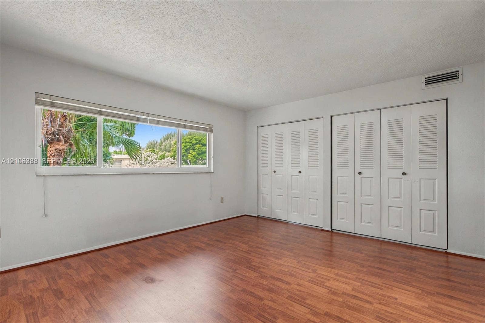 8110 SW 82nd Court, Miami, FL 33143 Room featuring wood-finish flooring, large horizontal window, and dual sets of white louvered-panel closet doors
