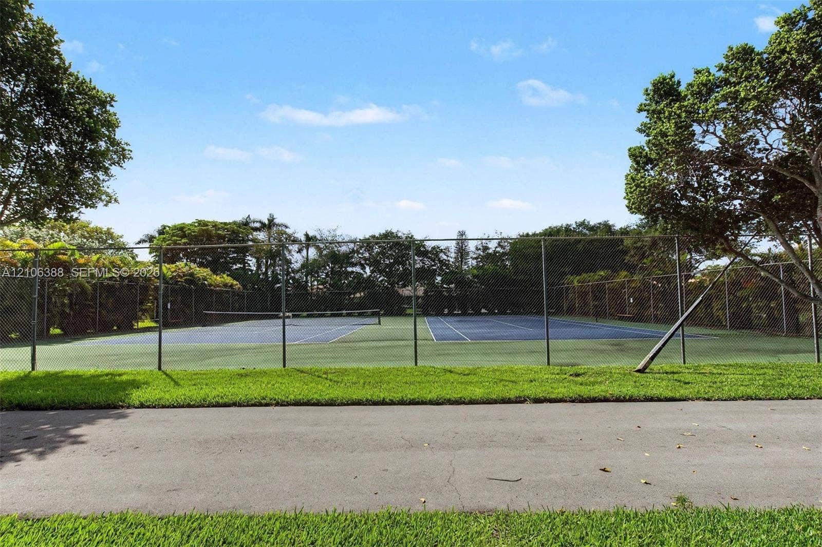 8110 SW 82nd Court, Miami, FL 33143 Tennis court featuring a paved surface, chain-link perimeter fencing, and mature surrounding trees