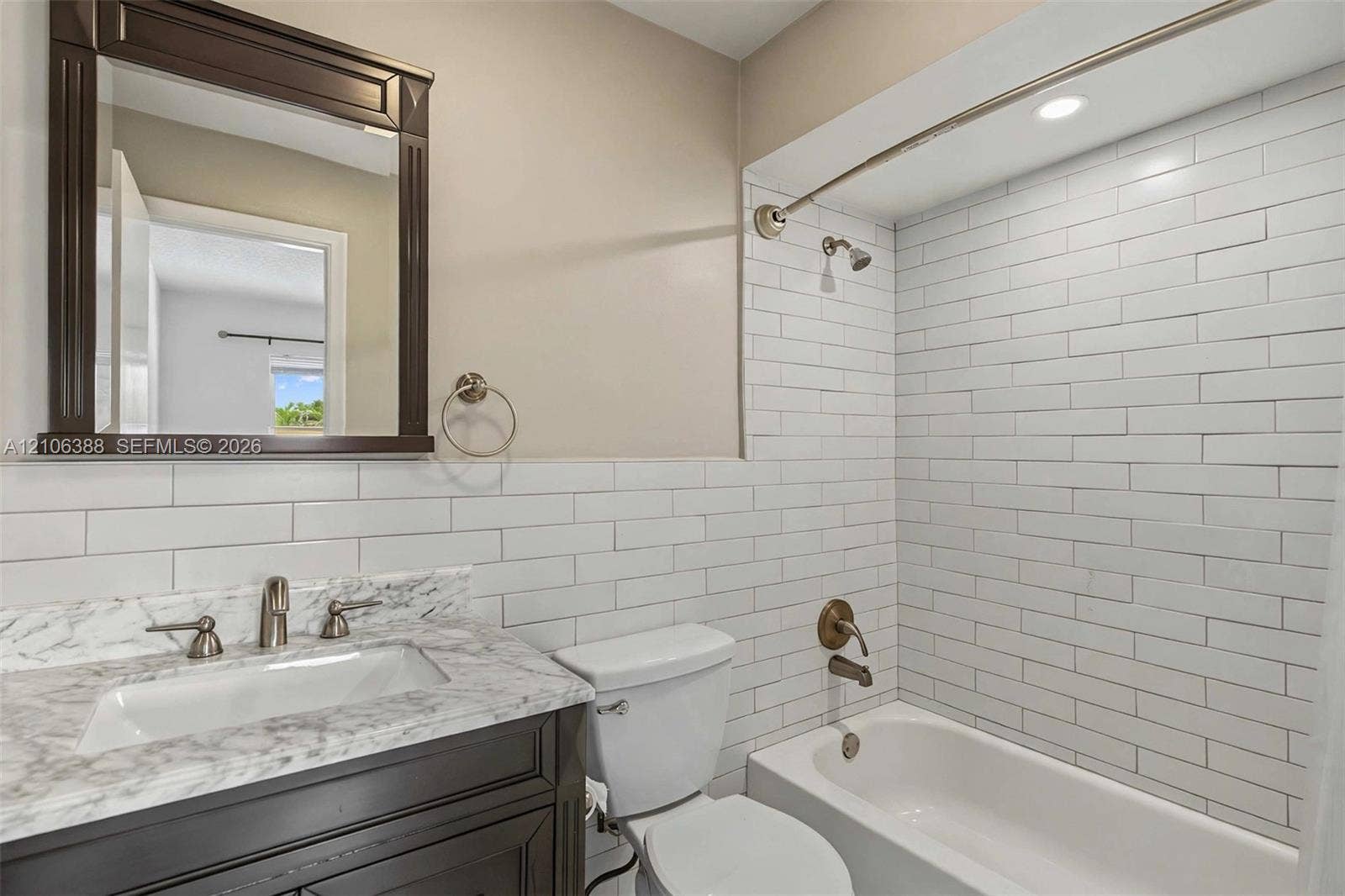 8110 SW 82nd Court, Miami, FL 33143 Bathroom featuring a dark wood vanity with a stone-finish countertop, undermount sink, white subway tile shower surround, and a framed mirror