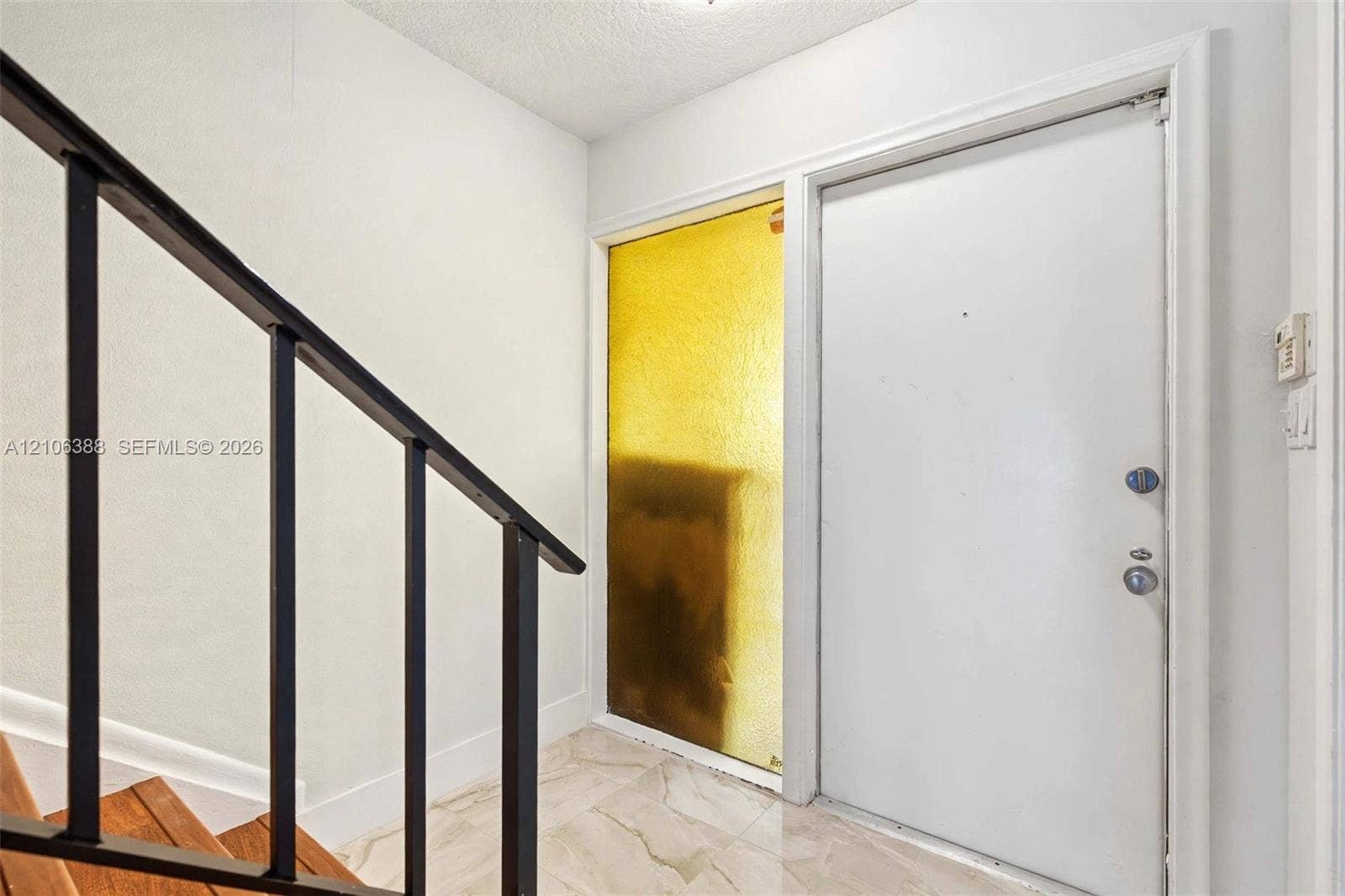 8110 SW 82nd Court, Miami, FL 33143 Entryway featuring a solid white door, a floor-to-ceiling amber-tinted sidelight, stone-finish tile flooring, and a metal staircase railing