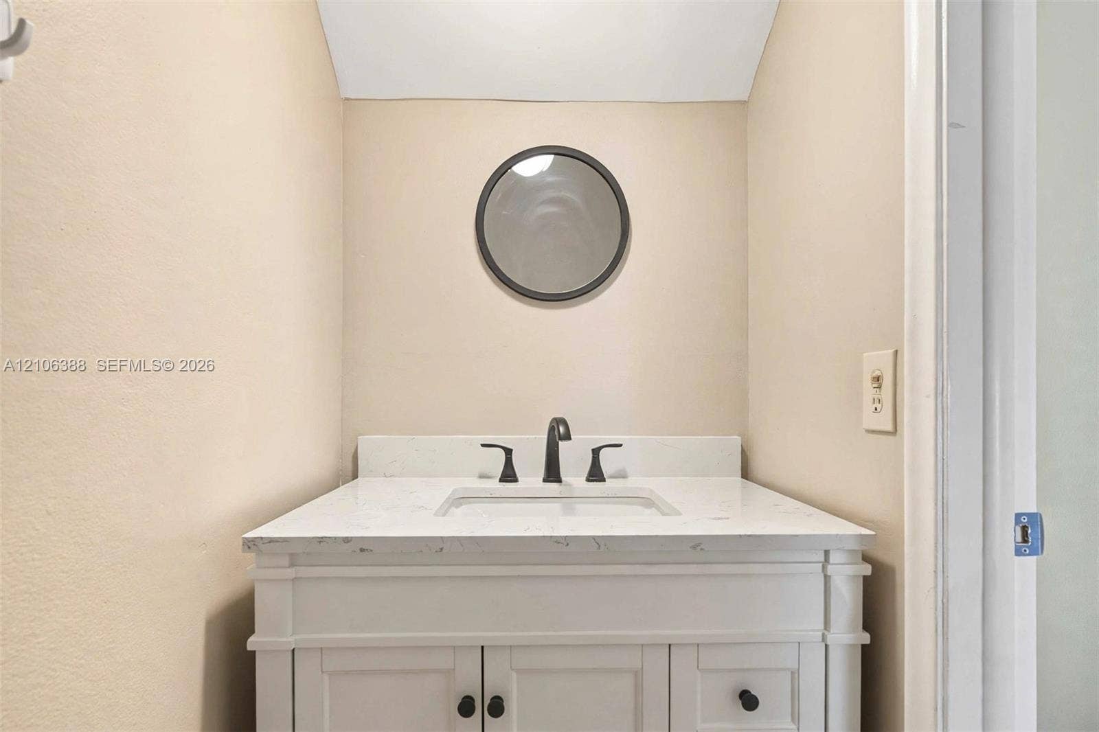 8110 SW 82nd Court, Miami, FL 33143 White vanity featuring a stone-surface countertop, an integrated rectangular sink, matte black widespread faucet hardware, and a circular mirror with a dark frame