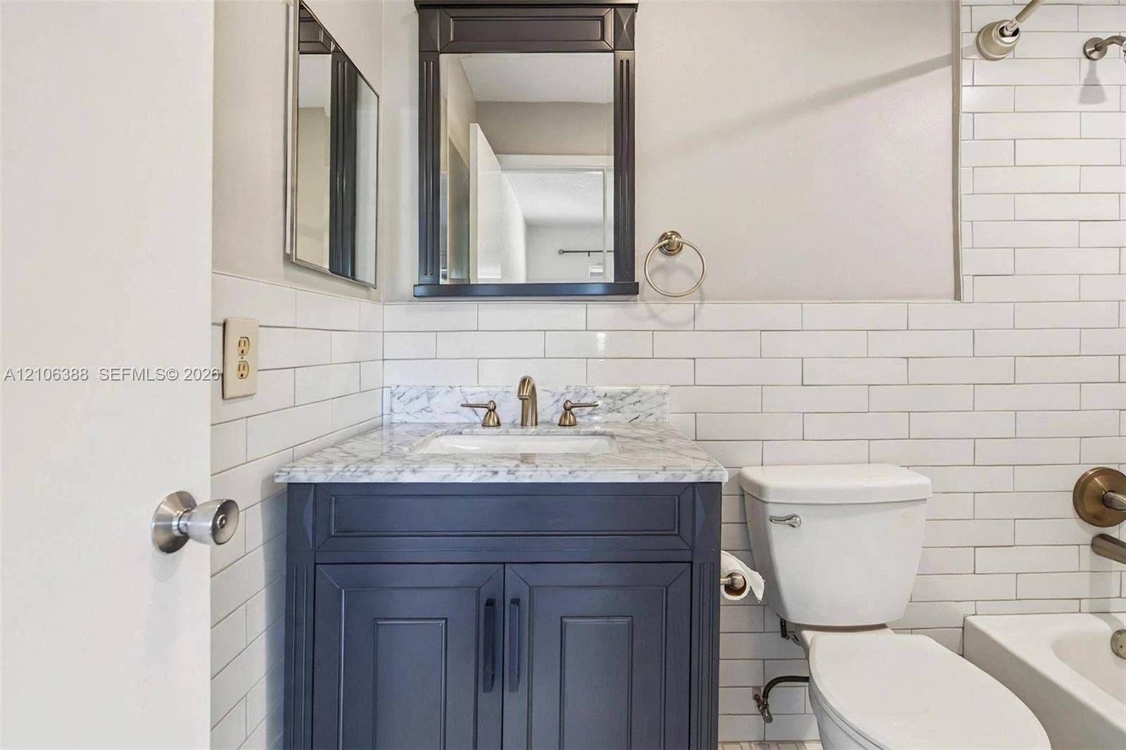 8110 SW 82nd Court, Miami, FL 33143 Bathroom featuring a navy blue vanity with stone-finish countertop, integrated under-mount sink, white subway-style tile wall surround, and framed mirror