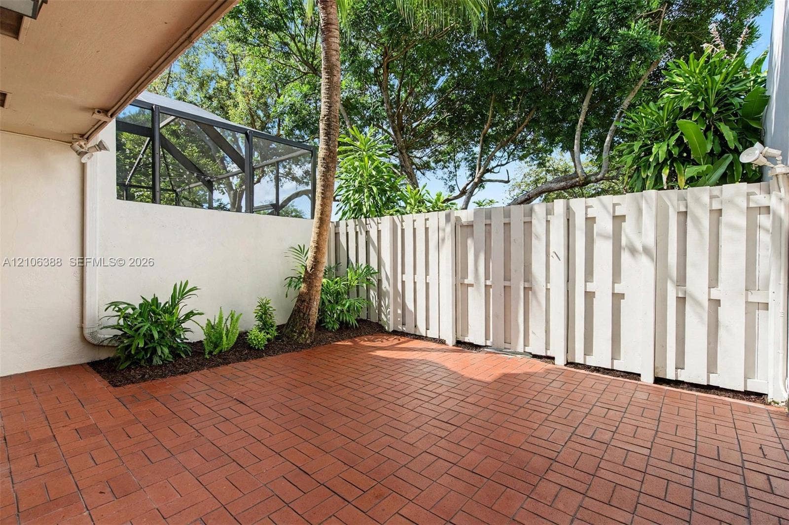 8110 SW 82nd Court, Miami, FL 33143 Private patio featuring red brick pavers, a white wood-style privacy fence, and mature landscaping