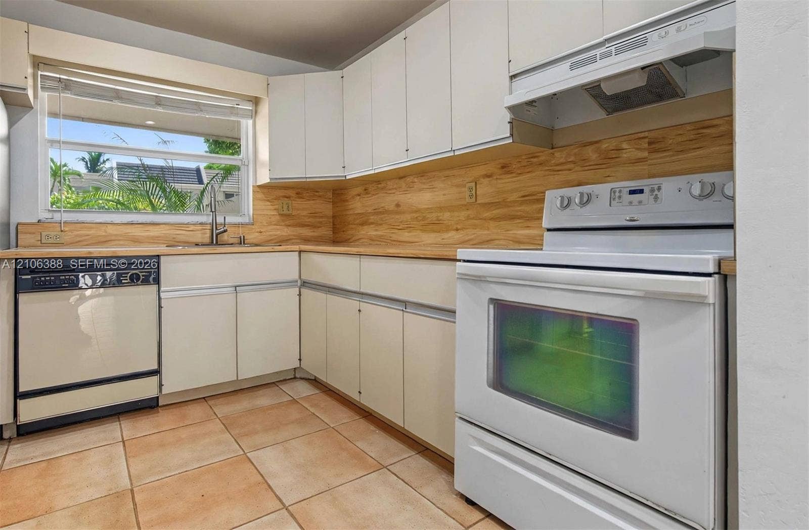 8110 SW 82nd Court, Miami, FL 33143 Kitchen featuring white cabinetry, light wood-tone backsplash, integrated range hood, ceramic tile flooring, and a stainless steel kitchen faucet