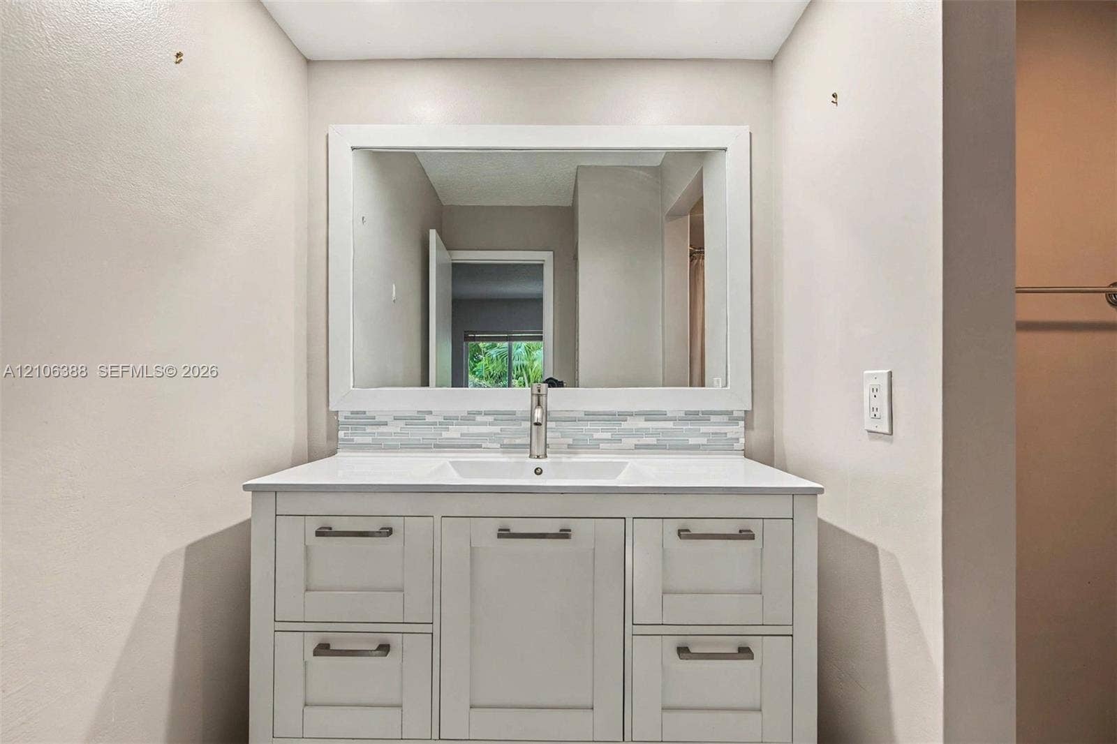 8110 SW 82nd Court, Miami, FL 33143 White cabinetry vanity featuring a rectangular integrated sink, white countertop, linear tile backsplash, and a framed mirror