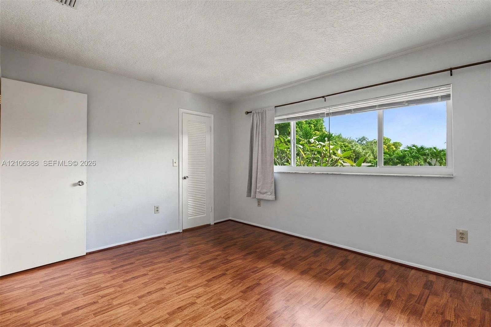8110 SW 82nd Court, Miami, FL 33143 Room featuring wood-finish flooring, a large horizontal window with exterior foliage, and louvered closet door