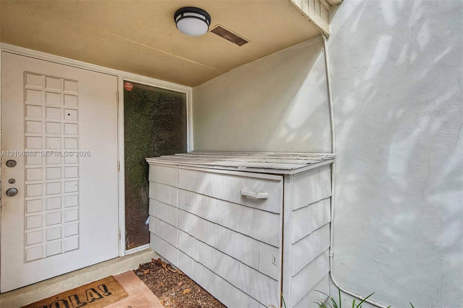 8110 SW 82nd Court, Miami, FL 33143 Entryway featuring a solid door with decorative recessed panels, a textured glass sidelight, exterior shiplap-style storage unit, and a flush-mount circular ceiling fixture