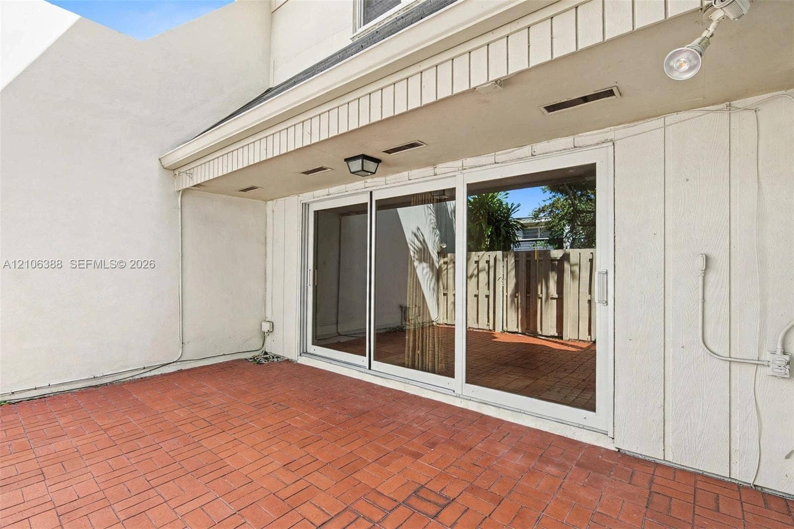8110 SW 82nd Court, Miami, FL 33143 Private patio featuring red brick paving, a three-panel sliding glass door, and a covered entryway with integrated lighting
