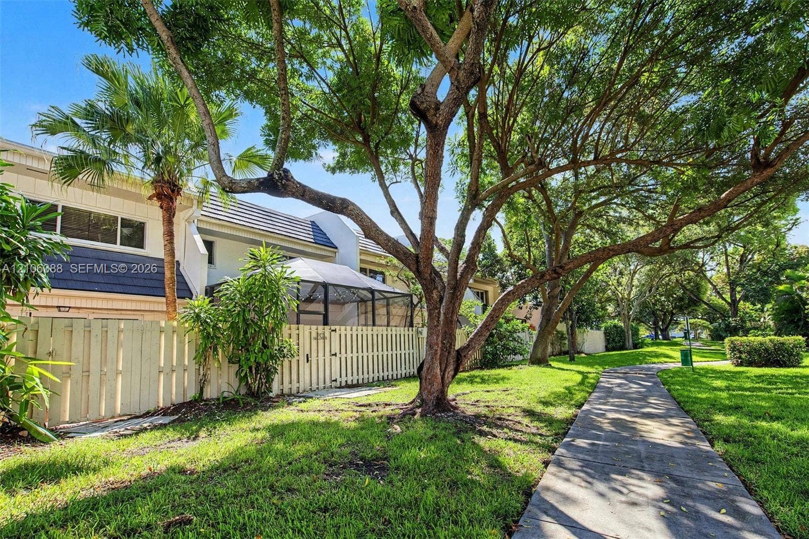 8110 SW 82nd Court, Miami, FL 33143 Exterior featuring a fenced-in patio with a screen enclosure, concrete walkway, mature trees, and landscaping