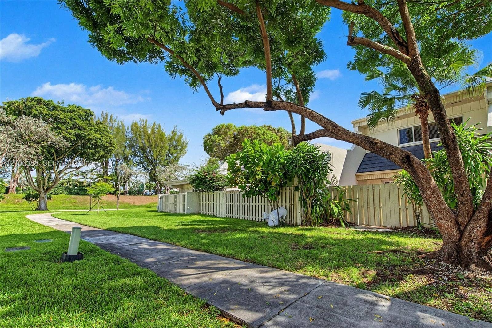 8110 SW 82nd Court, Miami, FL 33143 Manicured lawn featuring mature shade trees, a concrete pathway, and perimeter wood privacy fencing