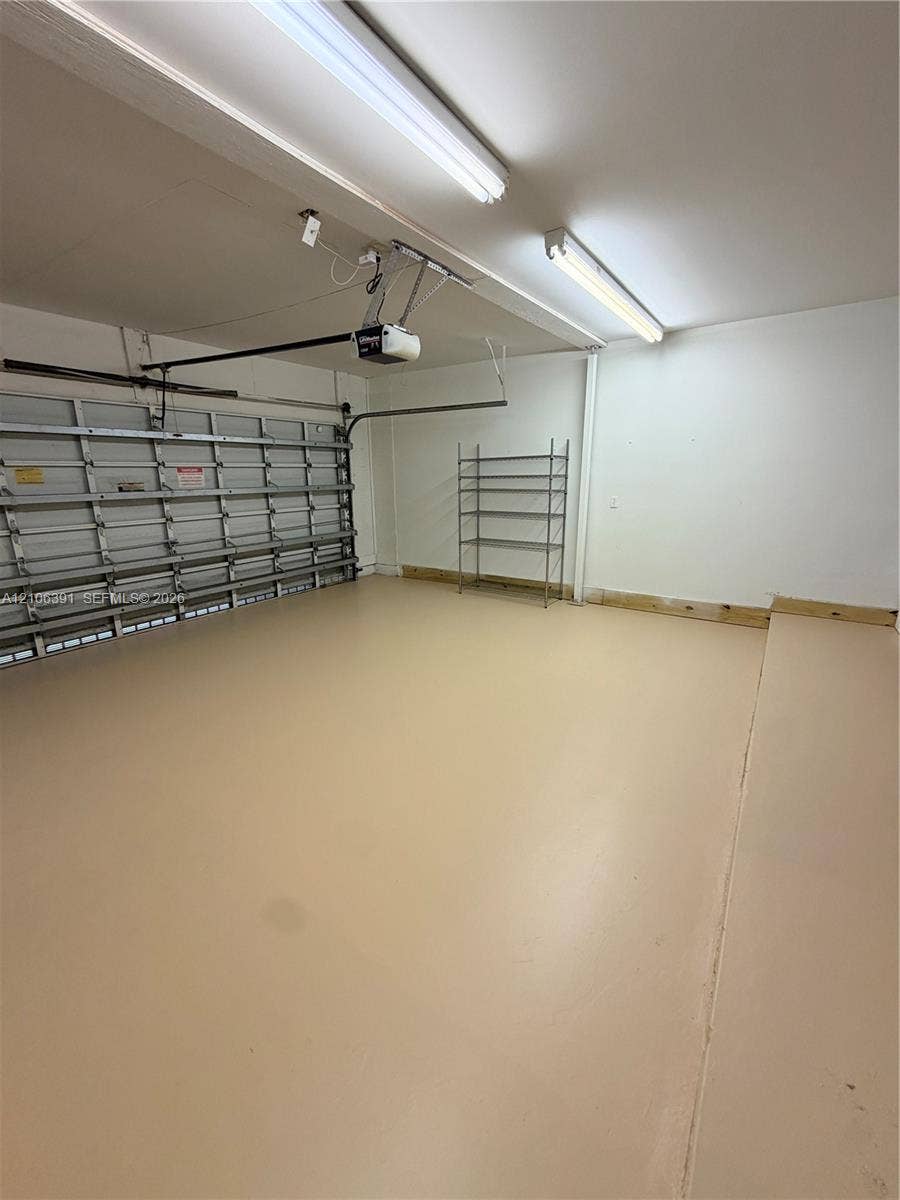 Finished garage interior featuring smooth-surface flooring, dual overhead fluorescent lighting, and an automated door opener mechanism