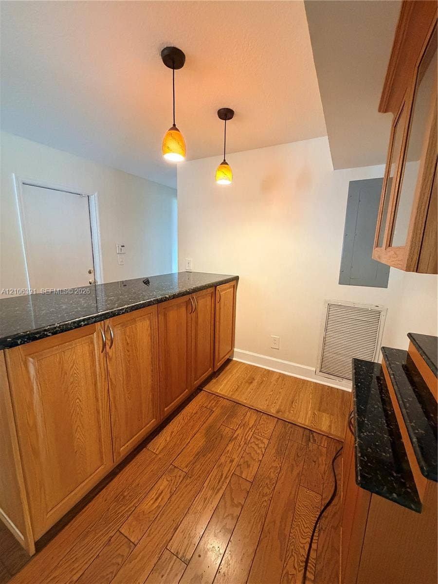 Wood-finish cabinetry paired with dark stone countertops, complemented by wood-finish flooring and dual amber-toned pendant lighting