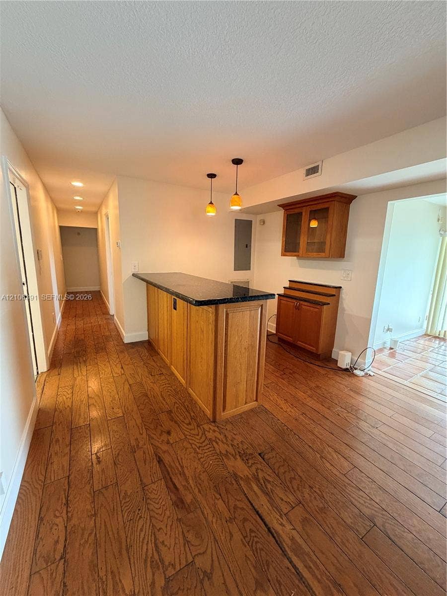 Wood-finish flooring, built-in wooden cabinetry, stone-top breakfast bar, and pendant lighting