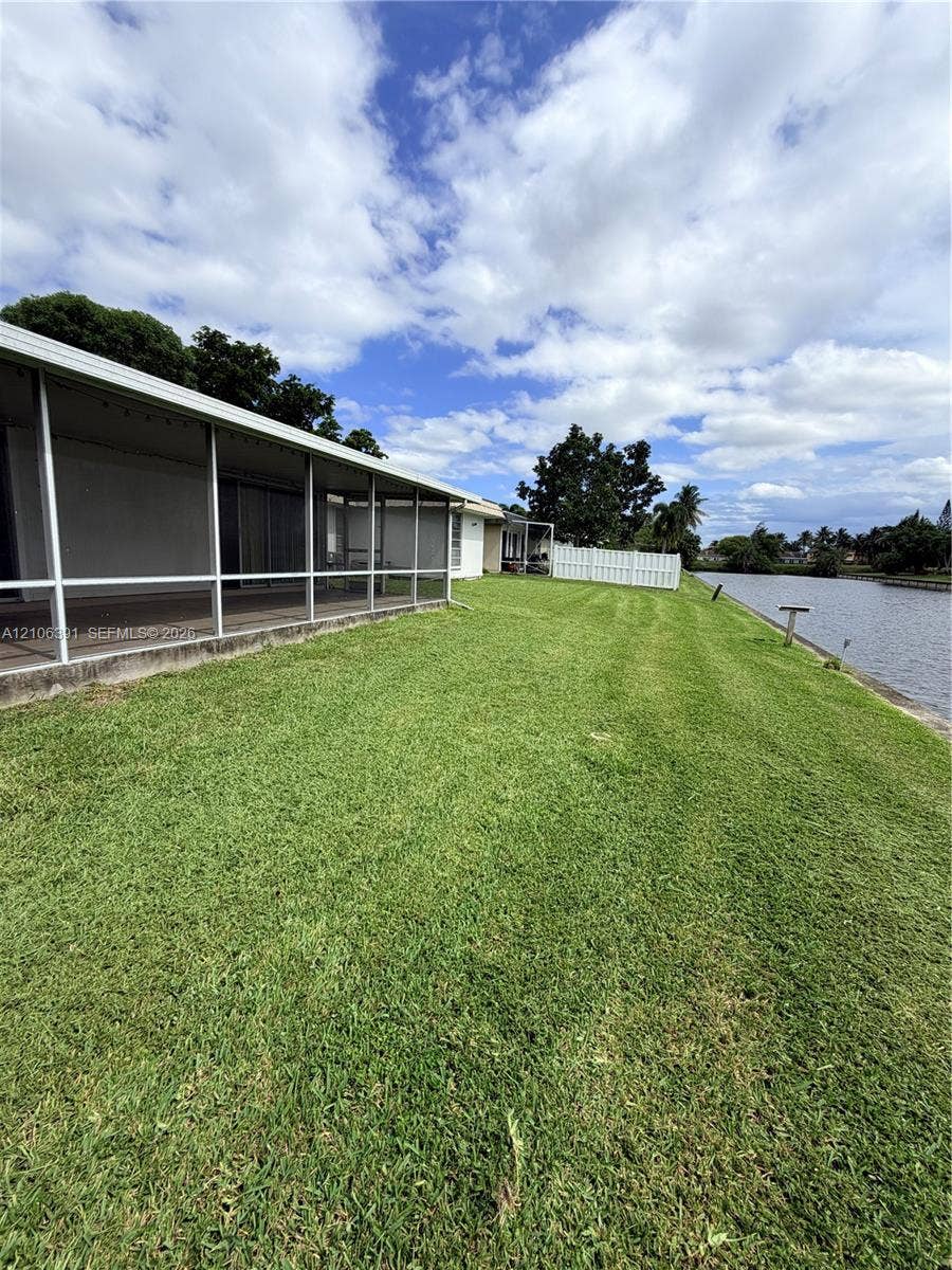 Screened-in rear porch with concrete flooring, expansive lawn, white vinyl fencing, and direct waterfront access