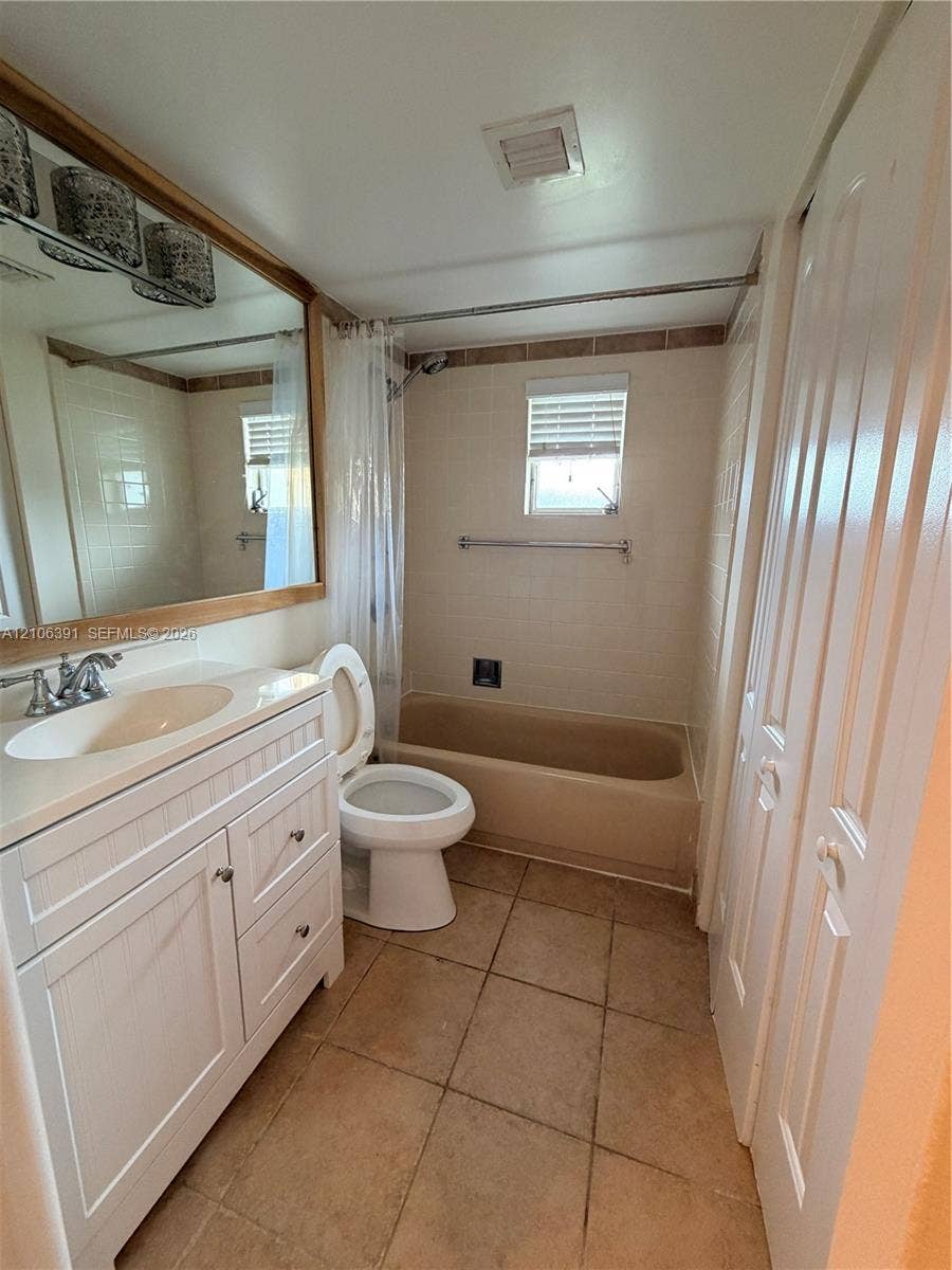 White wood-finish cabinetry featuring an integrated vanity, large wall-mounted mirror with wood-tone framing, tile flooring, and a bathtub with a tiled shower surround