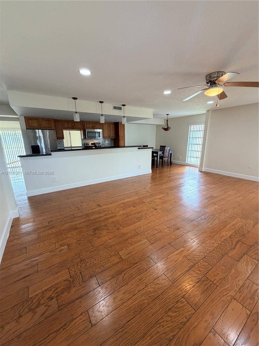 Open-concept interior featuring wood-finish flooring, a kitchen breakfast bar, recessed lighting, and a ceiling fan