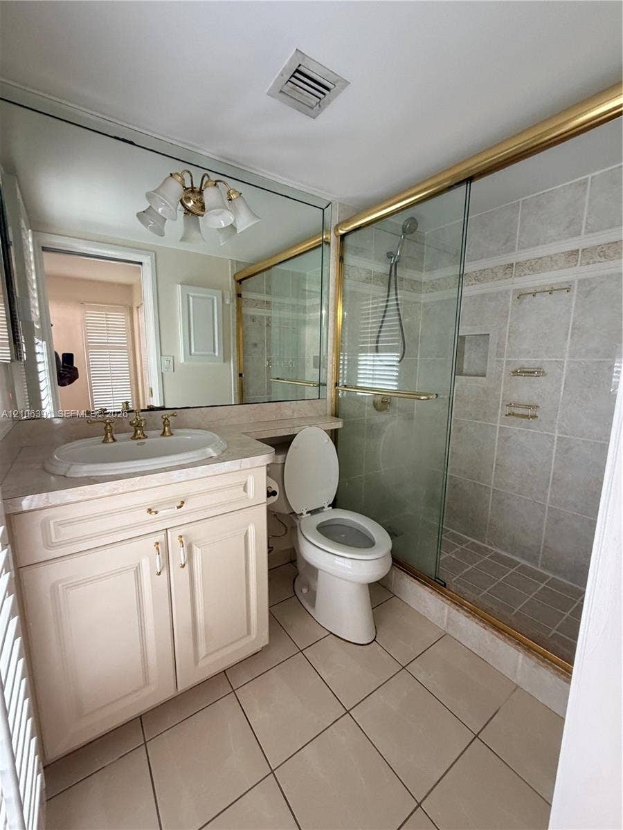 Bathroom featuring a single-sink vanity with stone countertop, tile-surround shower with glass enclosure, wall-to-wall mirror, and tile flooring