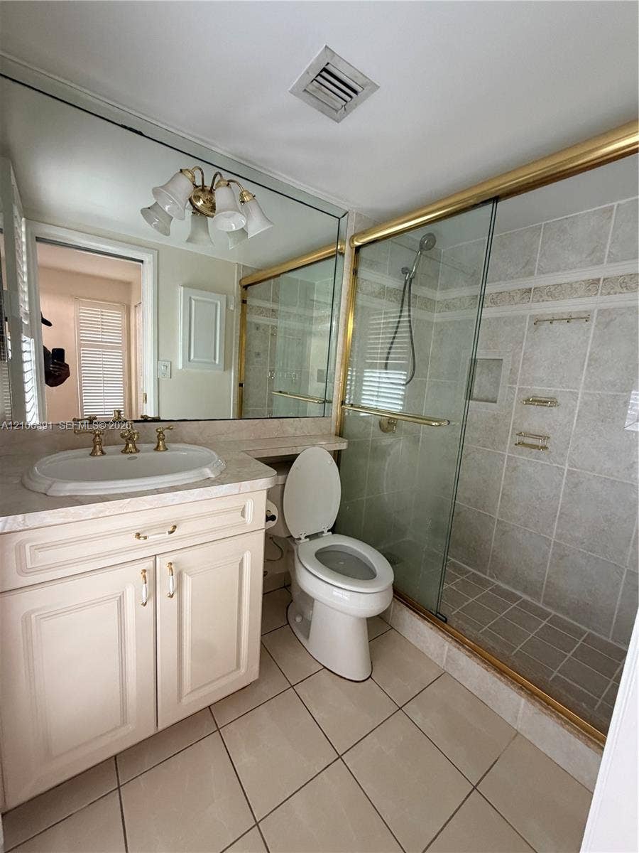 Bathroom featuring a vanity with integrated sink, brass-finish fixtures, full-width wall mirror, and a walk-in shower with glass enclosure