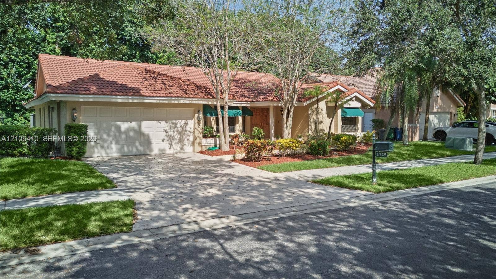 1725 Lakeshore Circle, Weston, FL 33326 Single-story exterior featuring a clay tile roof, stucco facade, two-car garage, and established landscaping