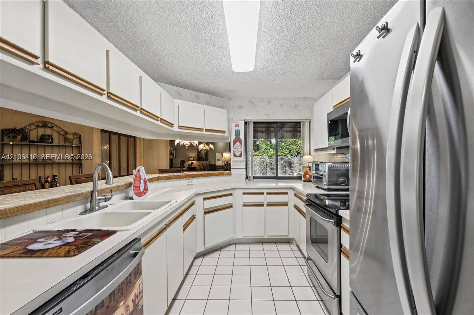 1725 Lakeshore Circle, Weston, FL 33326 Kitchen featuring white cabinetry, stainless steel appliances, a dual-basin sink with a gooseneck faucet, tile flooring, and a breakfast bar