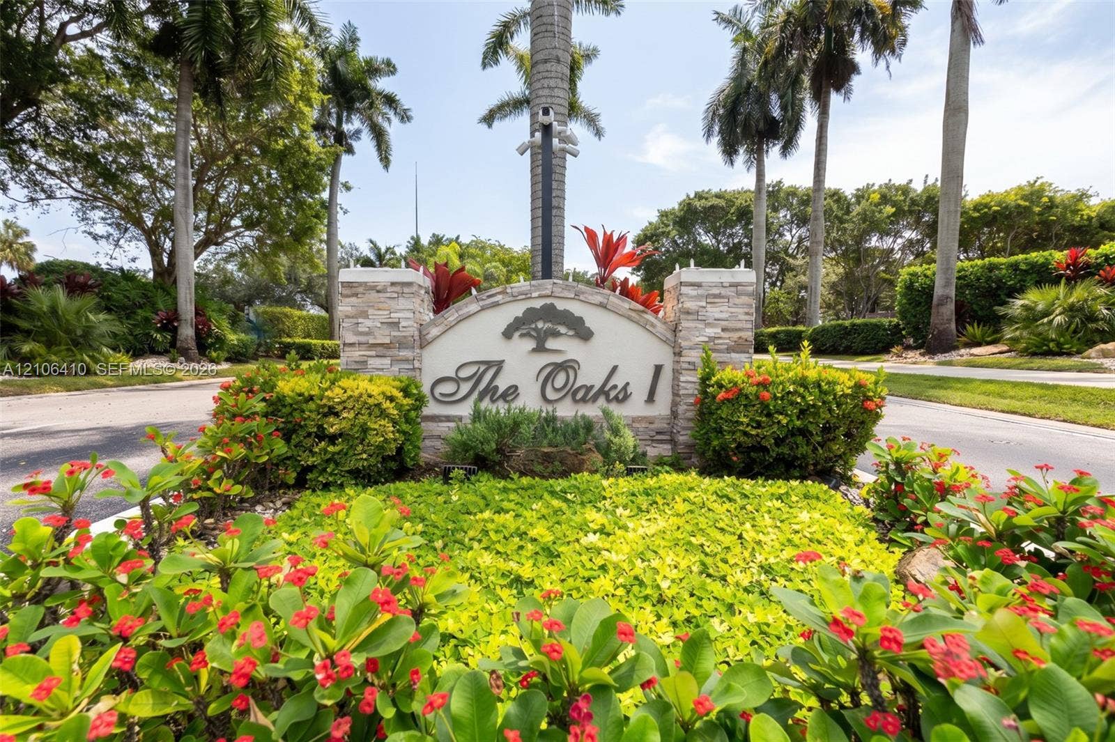 1725 Lakeshore Circle, Weston, FL 33326 Community entrance sign featuring stacked stone columns, a curved metal plaque, and surrounding mature landscaping with flowering shrubs and palm trees