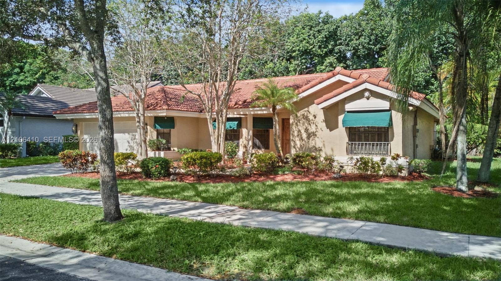 1725 Lakeshore Circle, Weston, FL 33326 Stucco exterior featuring a terracotta tile roof, fixed-frame window awnings, and landscaped garden beds