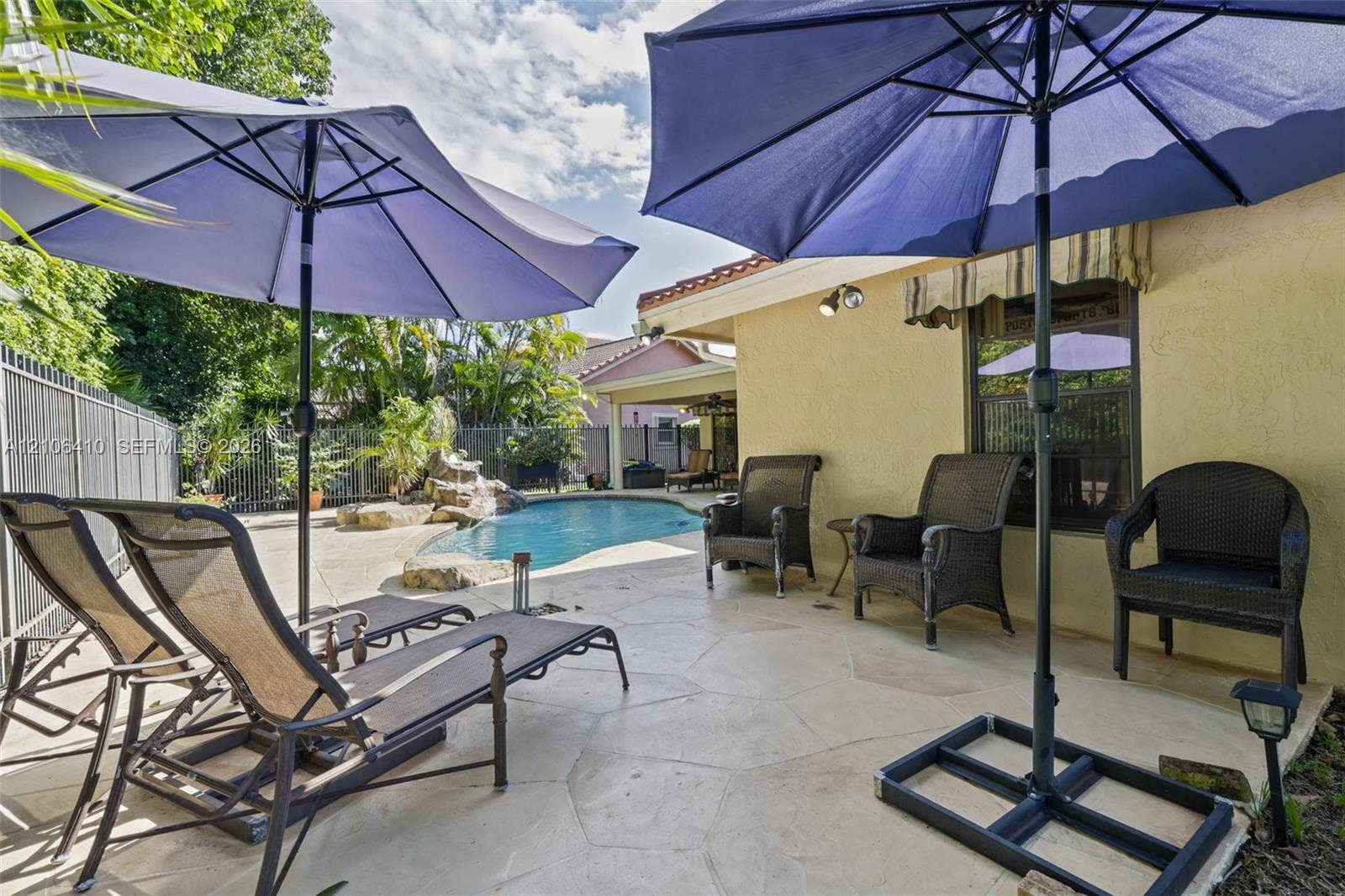 1725 Lakeshore Circle, Weston, FL 33326 Outdoor living area featuring a paved stone patio, a swimming pool with a rock-style water feature, and a stucco exterior finish