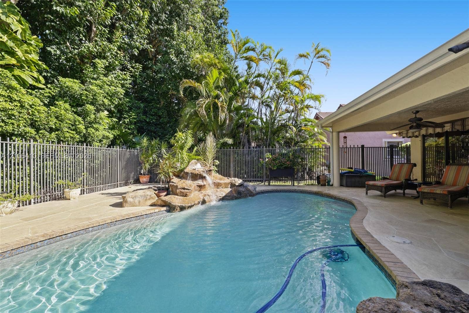 1725 Lakeshore Circle, Weston, FL 33326 Inground swimming pool with a stone water feature, covered patio, concrete deck, and metal perimeter fencing