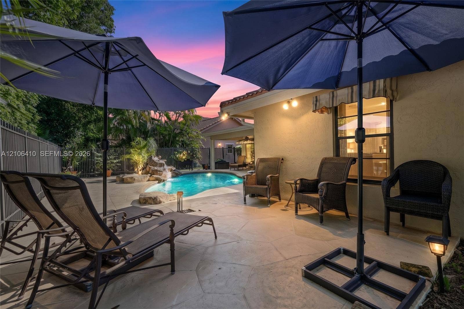 1725 Lakeshore Circle, Weston, FL 33326 Flagstone patio featuring an in-ground pool with a natural stone water feature, exterior wall-mounted lighting, and a metal perimeter fence