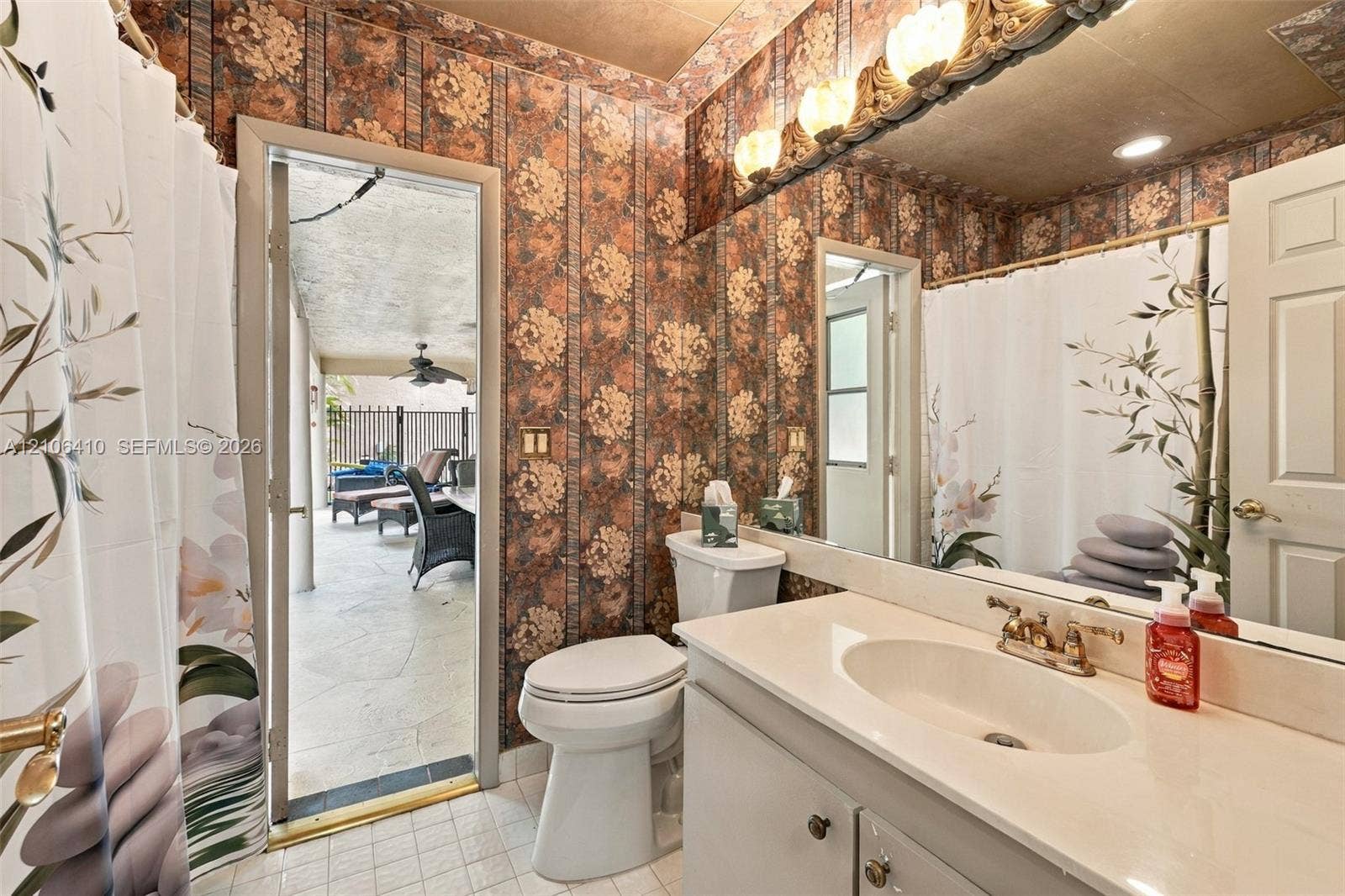1725 Lakeshore Circle, Weston, FL 33326 Bathroom featuring a solid-surface vanity countertop, drop-in sink with dual-handle faucet, full-width wall mirror, decorative light fixture, and tile flooring