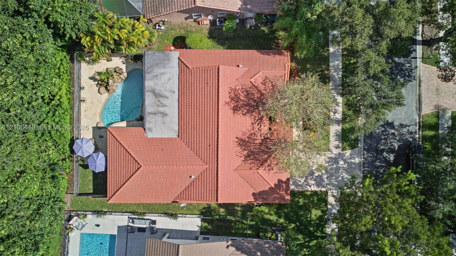 1725 Lakeshore Circle, Weston, FL 33326 Aerial perspective featuring a tile roof, an in-ground pool with a stone water feature, paved walkways, and mature landscaping