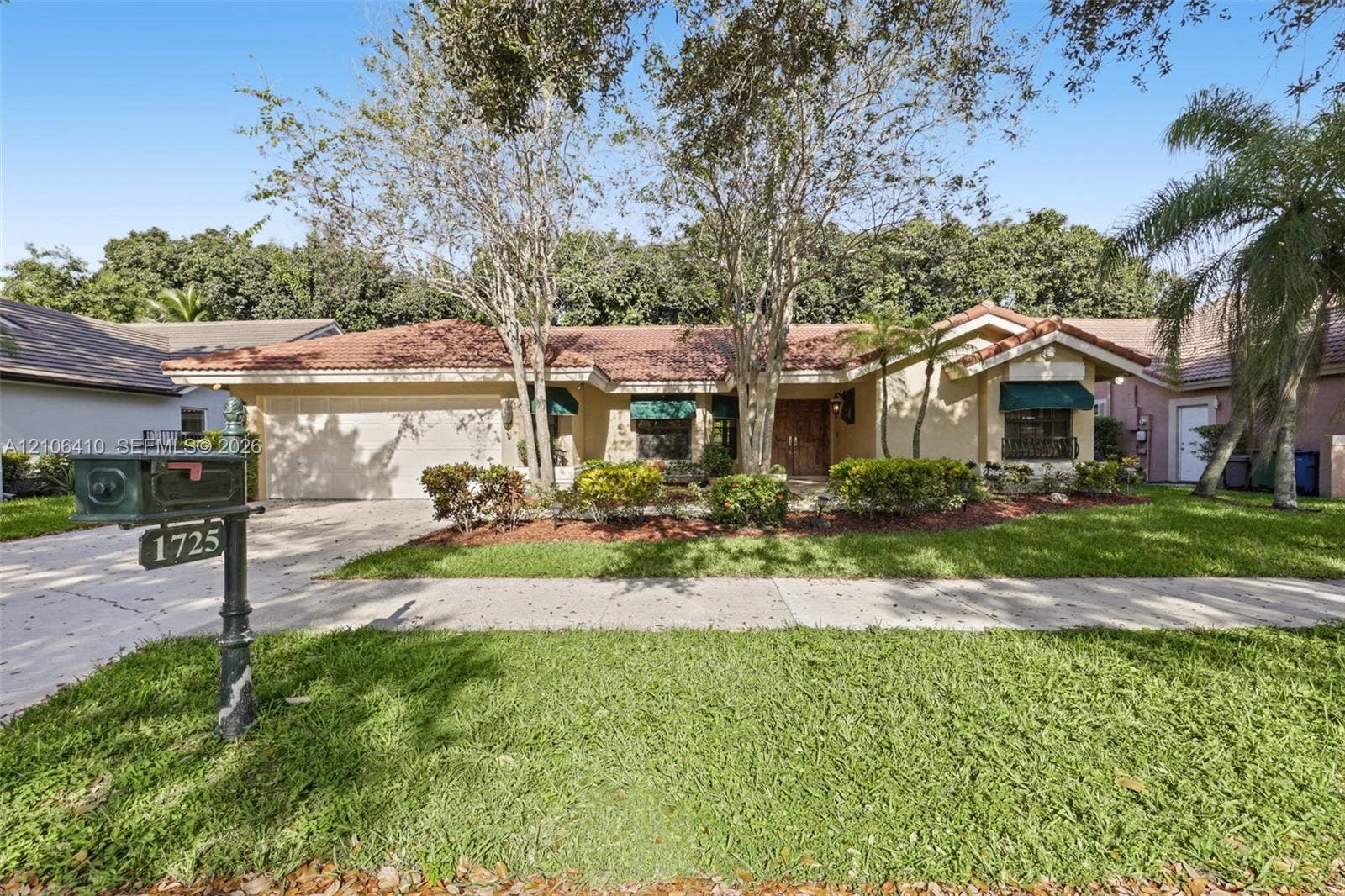 1725 Lakeshore Circle, Weston, FL 33326 Single-story exterior featuring a multi-gabled tile roof, stucco facade, attached two-car garage, and established landscaping with mature shade trees