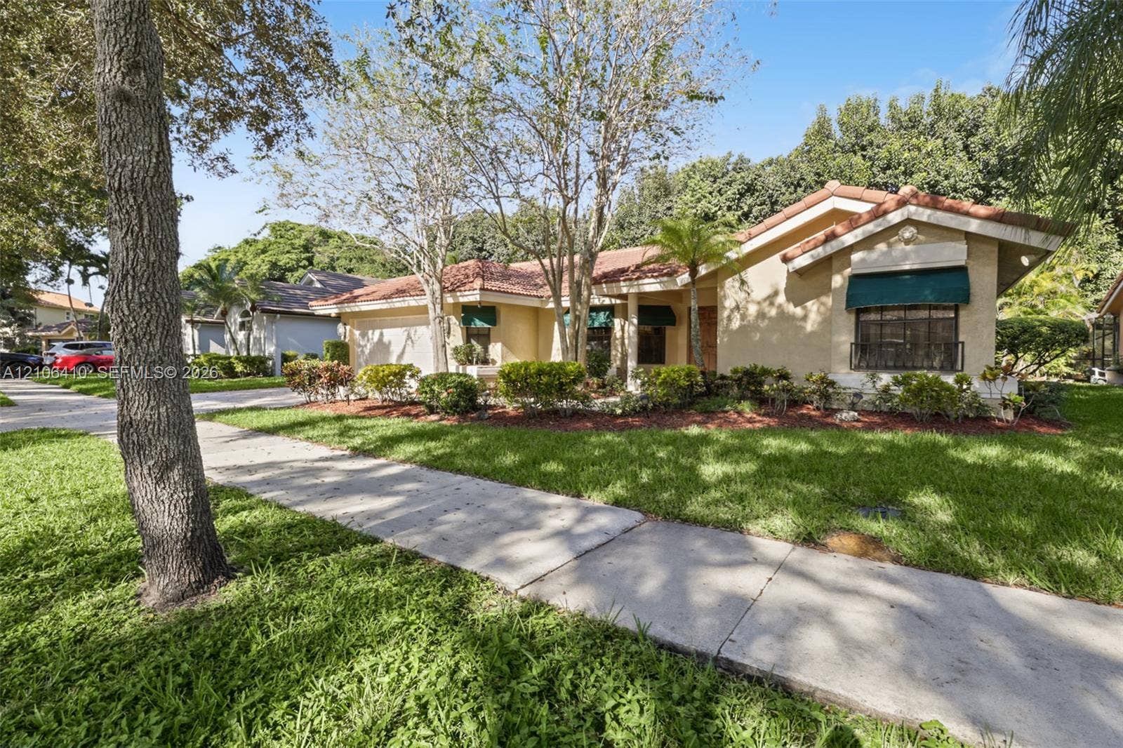 1725 Lakeshore Circle, Weston, FL 33326 Stucco exterior featuring a clay tile roof, attached garage, and decorative window awnings, complemented by established landscaping