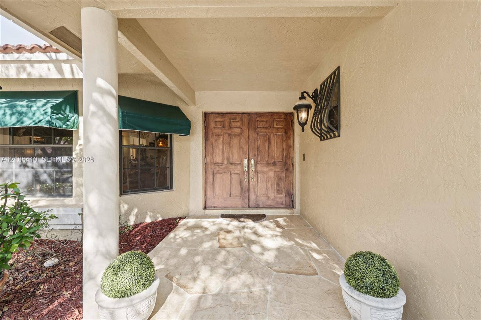 1725 Lakeshore Circle, Weston, FL 33326 Covered entryway featuring flagstone paving, double stained-wood doors, decorative wall-mounted lighting, and fabric window awnings