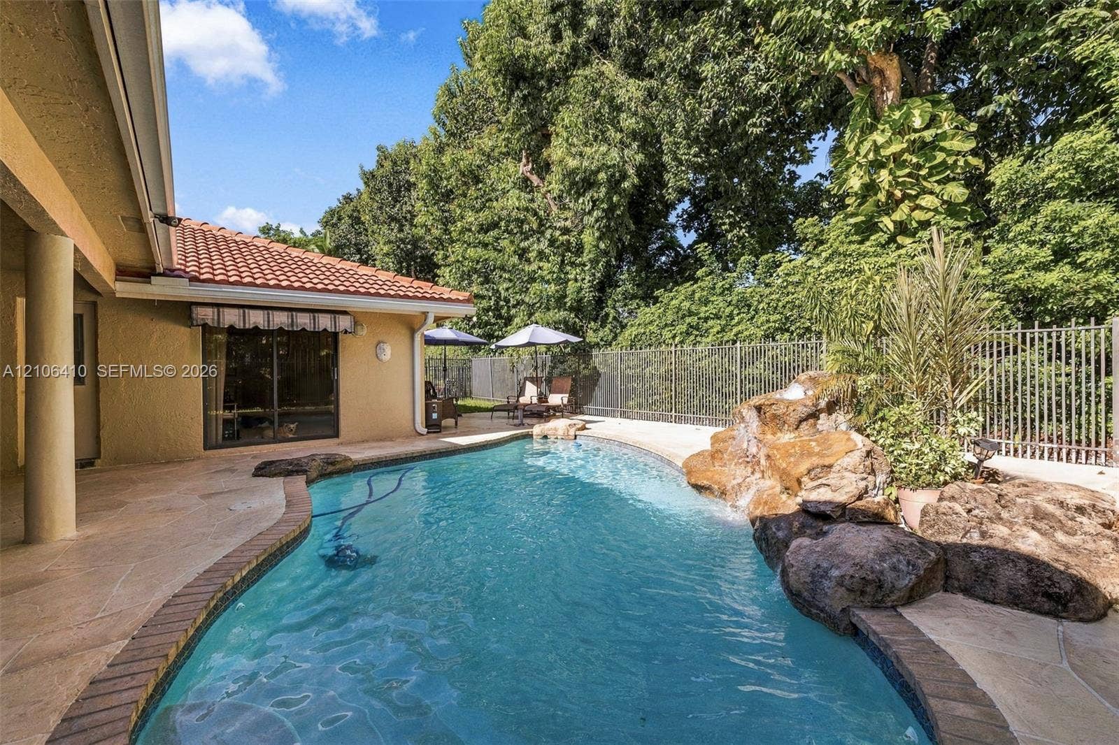 1725 Lakeshore Circle, Weston, FL 33326 Backyard featuring an inground pool with a rock water feature, stone-finished patio, tile roof, and metal perimeter fencing