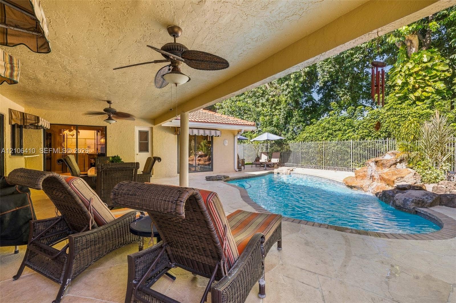 1725 Lakeshore Circle, Weston, FL 33326 Covered patio featuring a textured ceiling with integrated paddle fans, stone-paver decking, and a free-form pool with a rock water feature