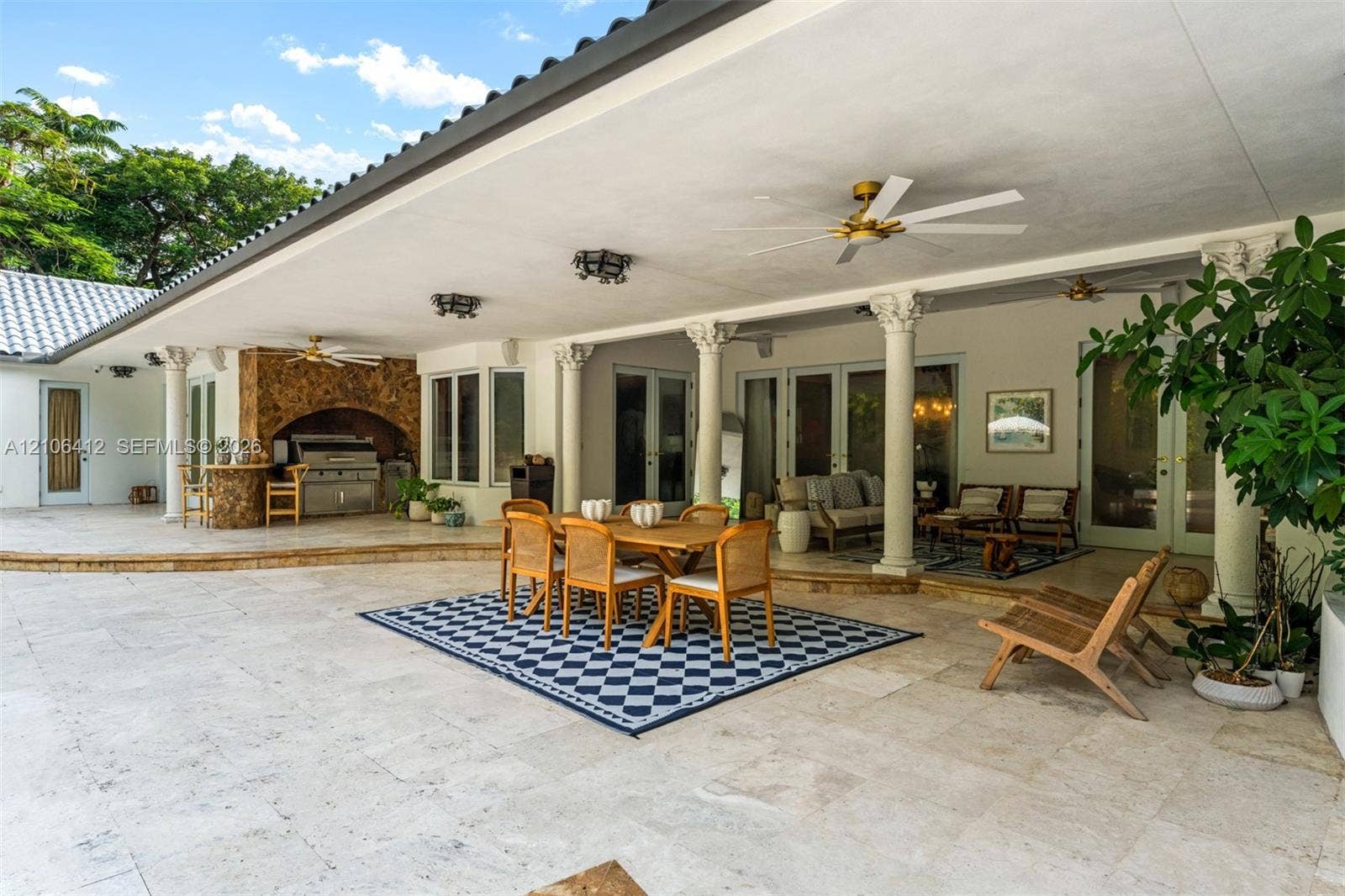 Covered patio featuring stone-tile flooring, decorative classical columns, a built-in outdoor kitchen, and dual ceiling fans