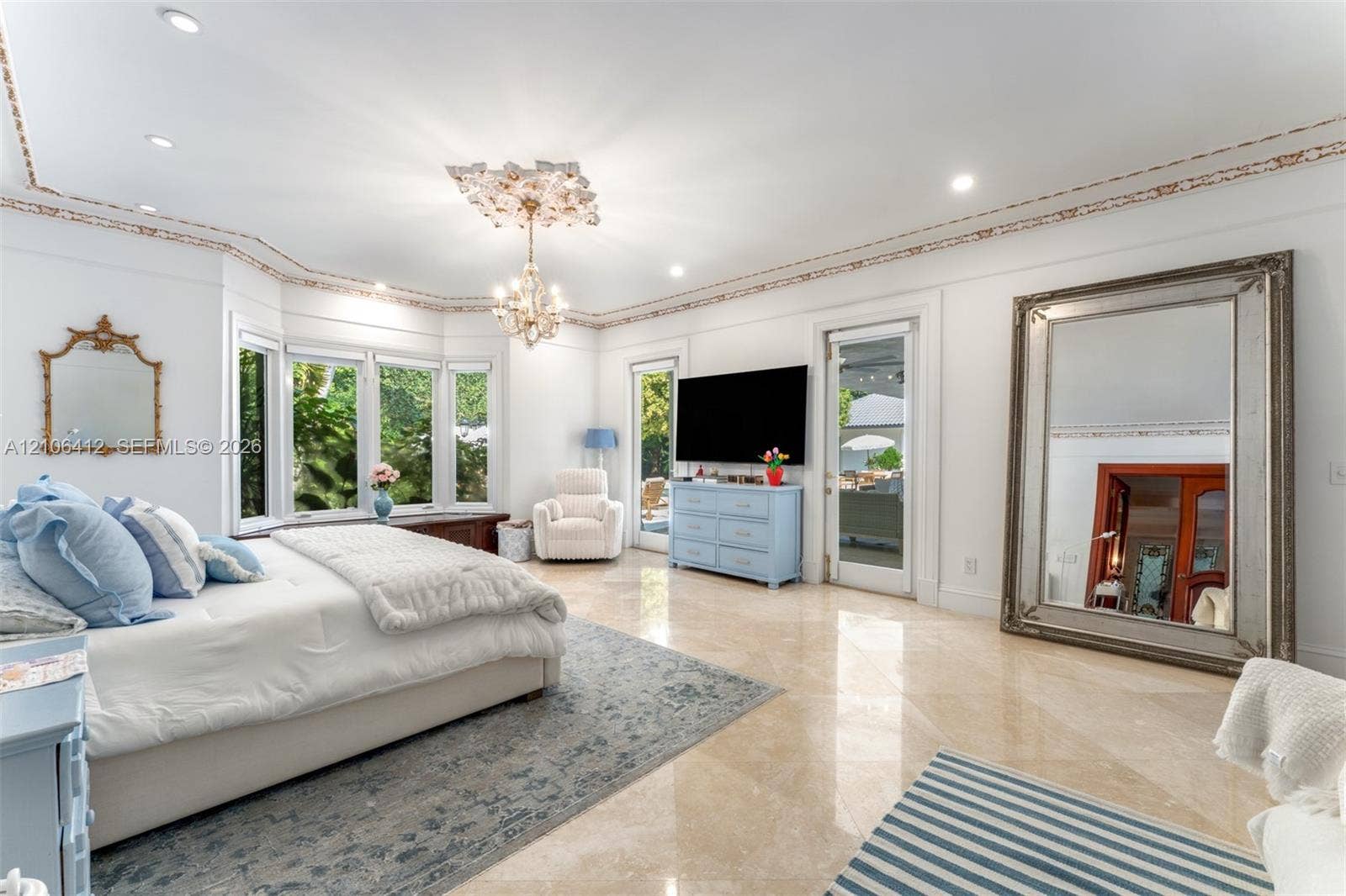 Spacious room featuring polished stone flooring, intricate crown molding, recessed lighting, a central crystal chandelier with a decorative ceiling medallion, and a curved bay window assembly