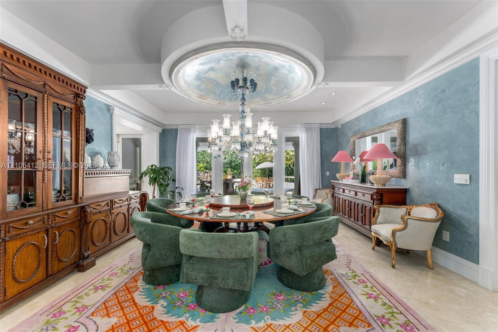 Formal dining room featuring a coffered ceiling with a recessed circular architectural detail, decorative wall finishes, built-in wooden cabinetry, a multi-tiered crystal chandelier, and glass-paned double doors