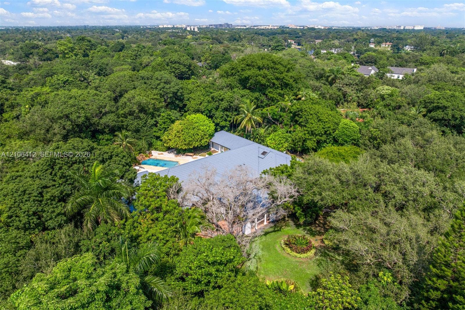 Aerial perspective of property featuring an expansive wooded lot, metal roofing, outdoor swimming pool, and professional landscaping