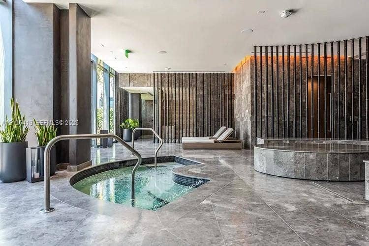 480 NE 31st Street, #1404, Miami, FL 33137 Indoor spa area featuring a built-in jetted tub with stainless steel handrails, circular cold plunge, floor-to-ceiling stone wall cladding, and vertical slat partitions