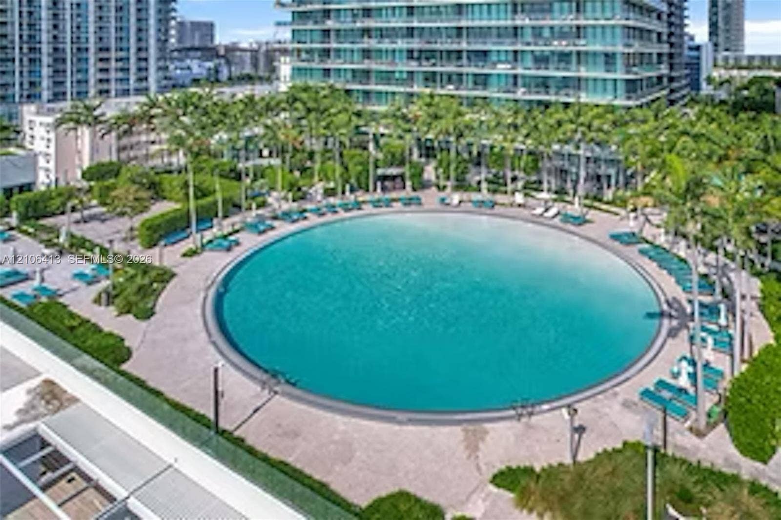 480 NE 31st Street, #1404, Miami, FL 33137 Circular swimming pool with a zero-entry edge, paved pool deck, and mature palm tree landscaping