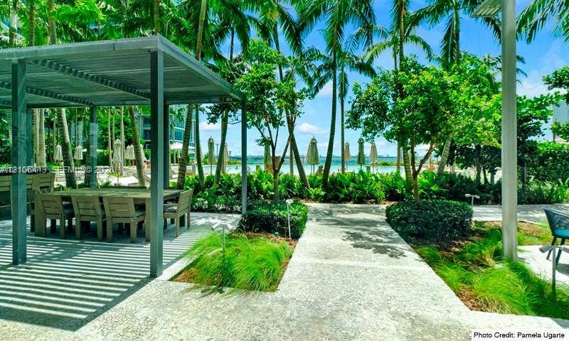 480 NE 31st Street, #1404, Miami, FL 33137 Outdoor patio area featuring a metal-frame pergola, stone-paved pathways, professional landscaping with mature palms, and built-in outdoor kitchen cabinetry
